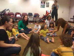 Crianças e adultos com camisetas brasileiras sentadas em roda no chão.